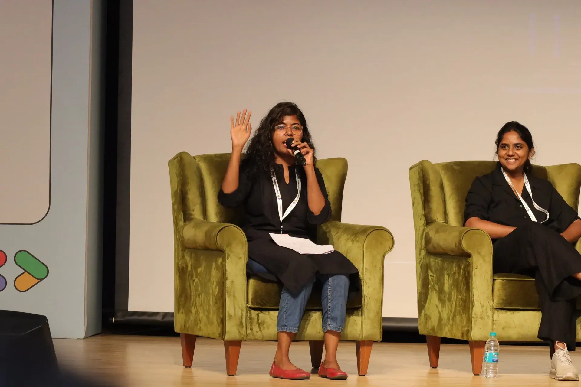 Two panellists seated on stage, one speaking into a handheld mic.
