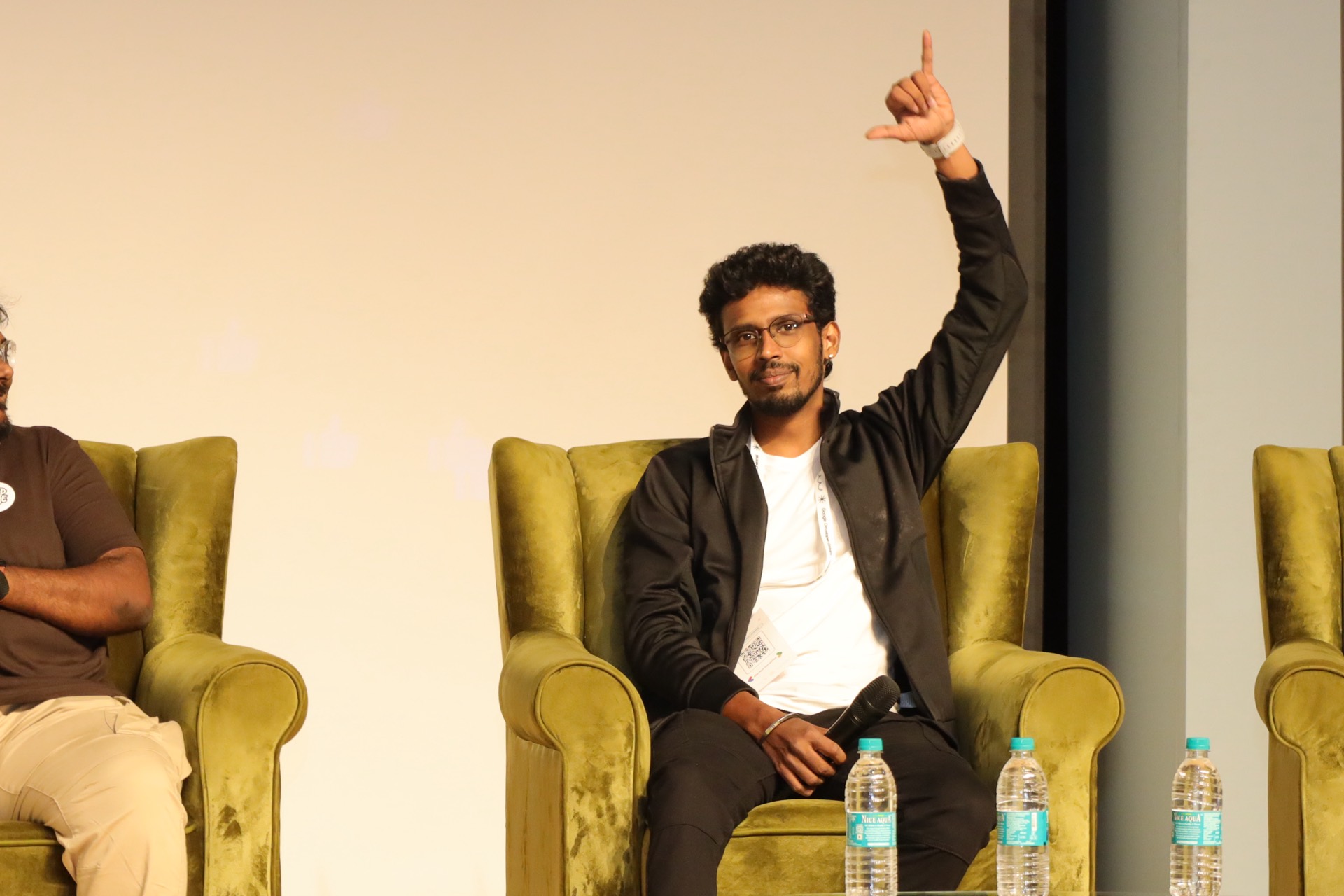 A panellist raising a hand to take a question from a green armchair on stage.