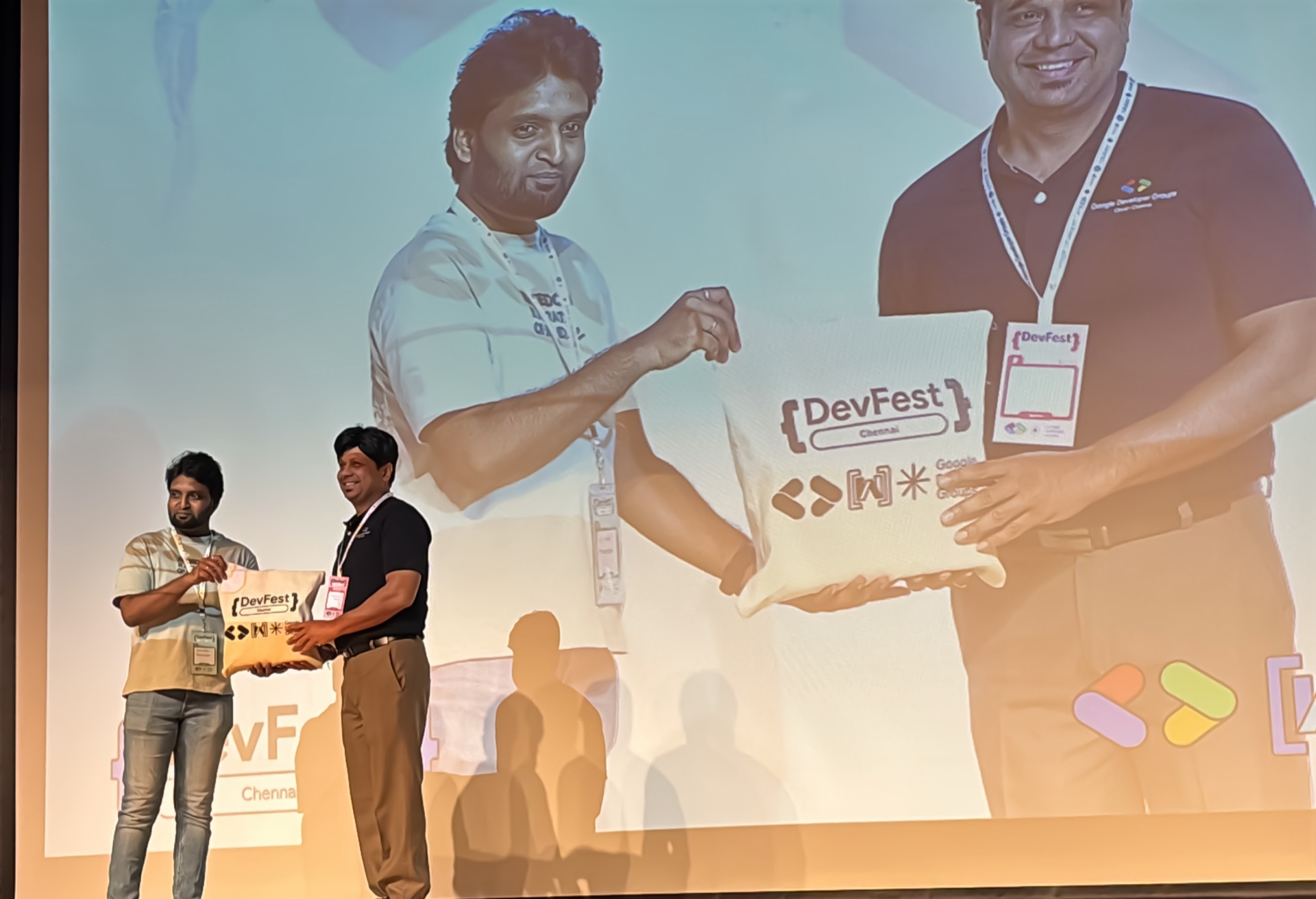 An organiser presenting a DevFest tote to a partner on stage.